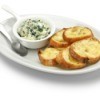 Dish of spinach artichoke dip and toasted baguette slices on a plate