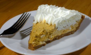 Slice of pumpkin mousse pie with whip cream and a fork on a white plate