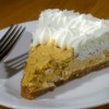 Slice of pumpkin mousse pie with whip cream and a fork on a white plate
