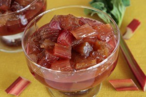 Bowl of ginger and orange rhubarb surrounded by pieces of uncooked rhubarb