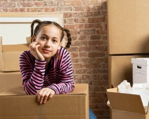 Young thoughtful girl resting with chin in hand amongst moving boxes