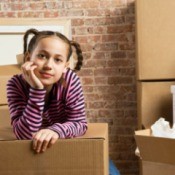 Young thoughtful girl resting with chin in hand amongst moving boxes