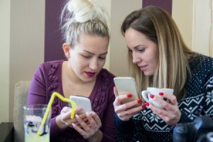 Two female friends looking at cell phones together.