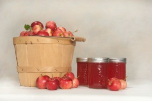 Basket of crab apples next to three jars of crab apple jelly and loose crab apples.