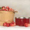 Basket of crab apples next to three jars of crab apple jelly and loose crab apples.