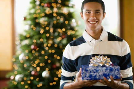 Teenage boy holding rapped Christmas present in front of decorated tree