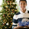 Teenage boy holding rapped Christmas present in front of decorated tree