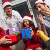 Four adults in santa hats laughing and exchanging brightly colored gifts