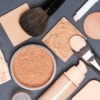 Various face powders and foundations with brushes displayed on grey surface