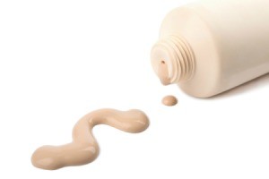 Liquid foundation bottle laying on side, with foundation spilled on white surface