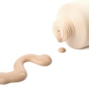 Liquid foundation bottle laying on side, with foundation spilled on white surface