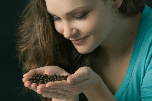 Woman with long hair smelling coffee beans in her cupped hands