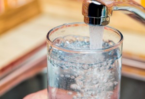 Clear drinking glass being filled with water from a kitchen faucet