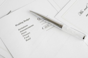 Paper labelled wedding budget with an items column next to a pen and wedding invitation