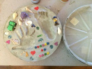 Using Flower Pot Saucers for Stepping Stones - Finished stepping stone with small toys around the hand and foot print.