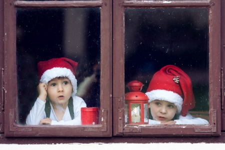 Two boys in santa hats looking out window in hopes of seeing Santa