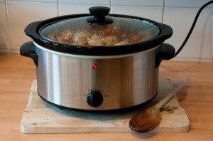 Crockpot plugged in and cooking meal on a wooden counter.