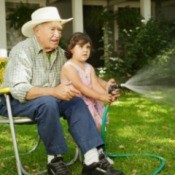 Grandfather sitting in chair and helping Granddaughter water the lawn