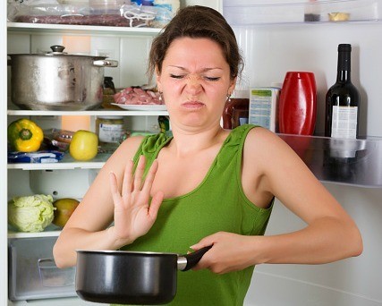 Woman with disgusted face by refrigerator