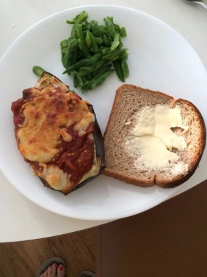 A plate with stuffed eggplant, greens and a slice of bread with butter.