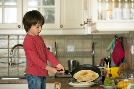 Young boy making crepes on the stove