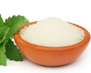 Bowl of Stevia granules next to a sprig of stevia leaf