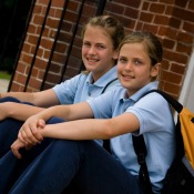 Two girls in private school uniforms sitting on steps in front of brick building