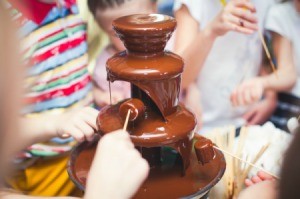 Chocolate fountain with people dipping marshmallows and fruit