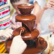 Chocolate fountain with people dipping marshmallows and fruit