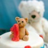 Cake with fondant teddy bear decoration and a teddy bear stuffed toy in the background