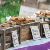 Plates of baked goods on crates with cards in front listing names and prices