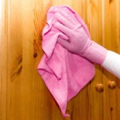 A hand in a pink glove cleaning wood cabinets.