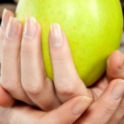 hands with long fingernails holding an apple