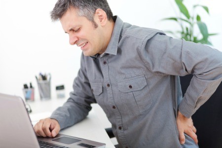 Man at computer grasping his back in pain