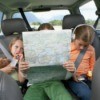 Three girls sitting the back seat of a car.  One is holding a map.