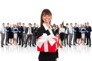 Woman in office attire holding out a wrapped gift with a row of people in suits in the background