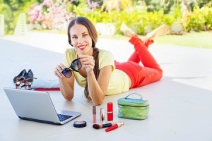 Woman lying on her belly in front of a laptop surrounded by cosmetics