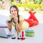 Woman lying on her belly in front of a laptop surrounded by cosmetics