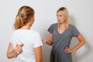 Girl arguing with her mother.  Mother is holding her hand out, girl has her fingers crossed behind her back