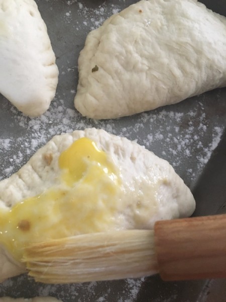 Brushing the tops of empanadas before baking.