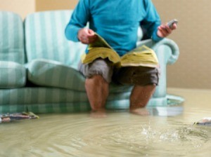 Man sitting on couch looking through phone book in flooded room with water up past his ankles