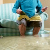 Man sitting on couch looking through phone book in flooded room with water up past his ankles