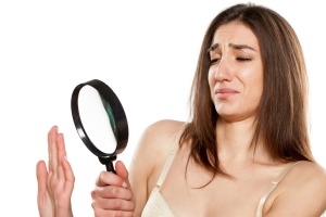 Woman looking at nails through a magnifying glass with distaste