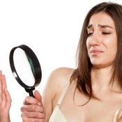 Woman looking at nails through a magnifying glass with distaste