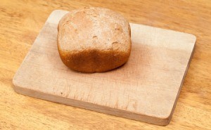 Loaf of bread machine bread that has not risen on a cutting board.