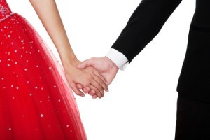 Close up of couple holding hands. Boy is in suit, girl is in a red sparkly party dress