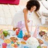 Overhead view of a woman setting up a birthday party table with bright colors candy, treats, and cake