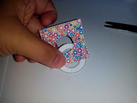 Hand holding colored paper square with center of frame removed ready to glue together.