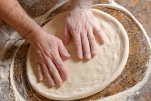 hands patting out pizza dough