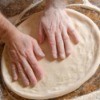 hands patting out pizza dough